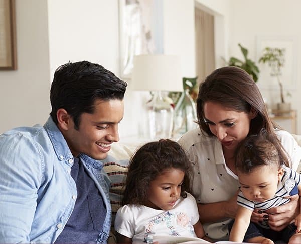 Parents reading to 2 small children on a comfy white couch.