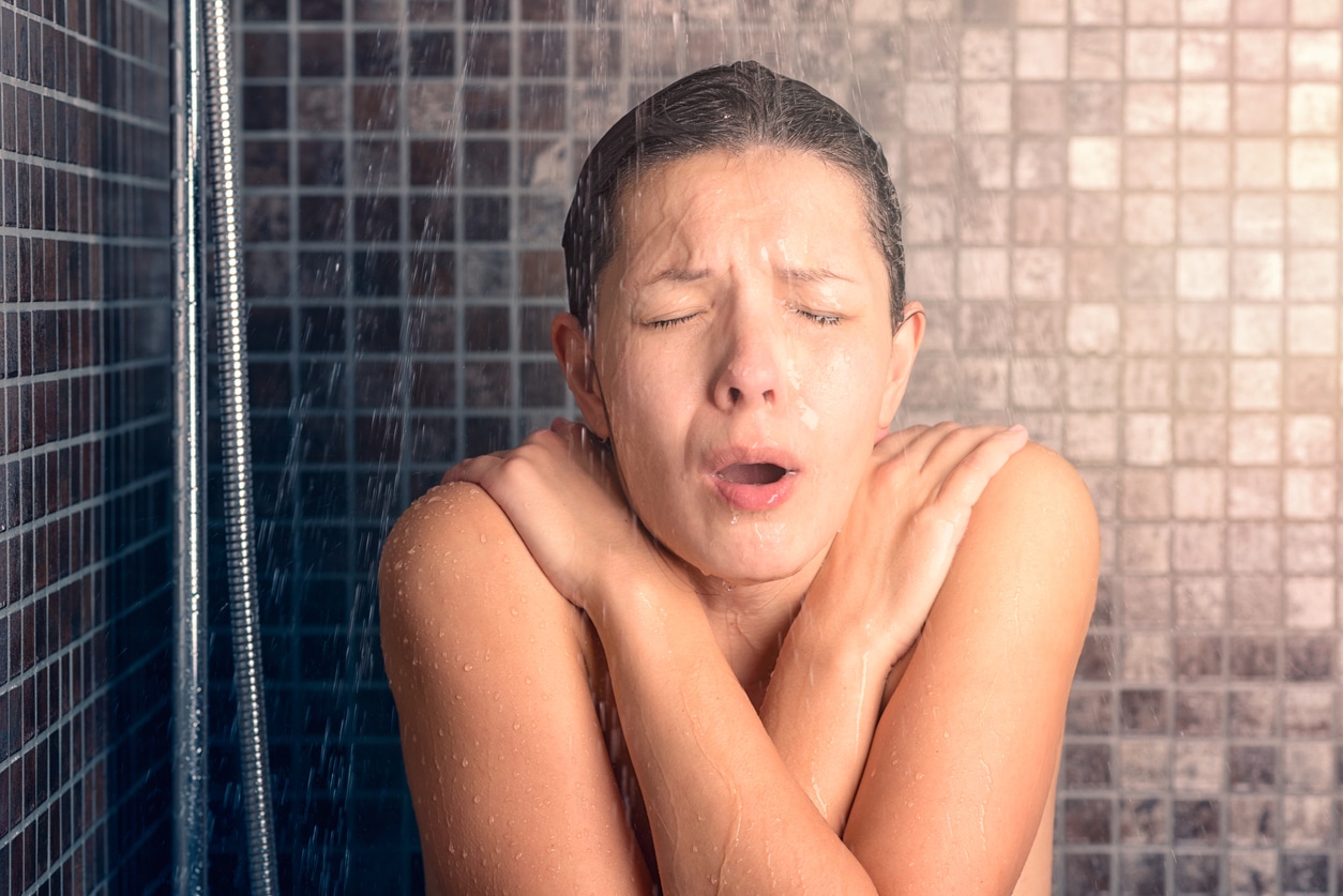 Woman taking a cold shower because her water heater does not work and heating water is it's primary role